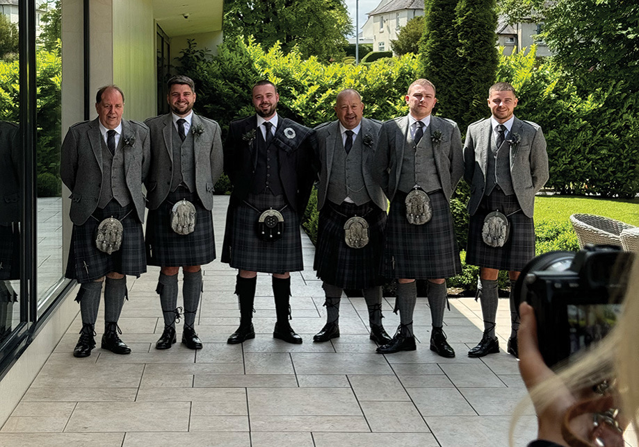 Six groomsmen in kilts standing outside